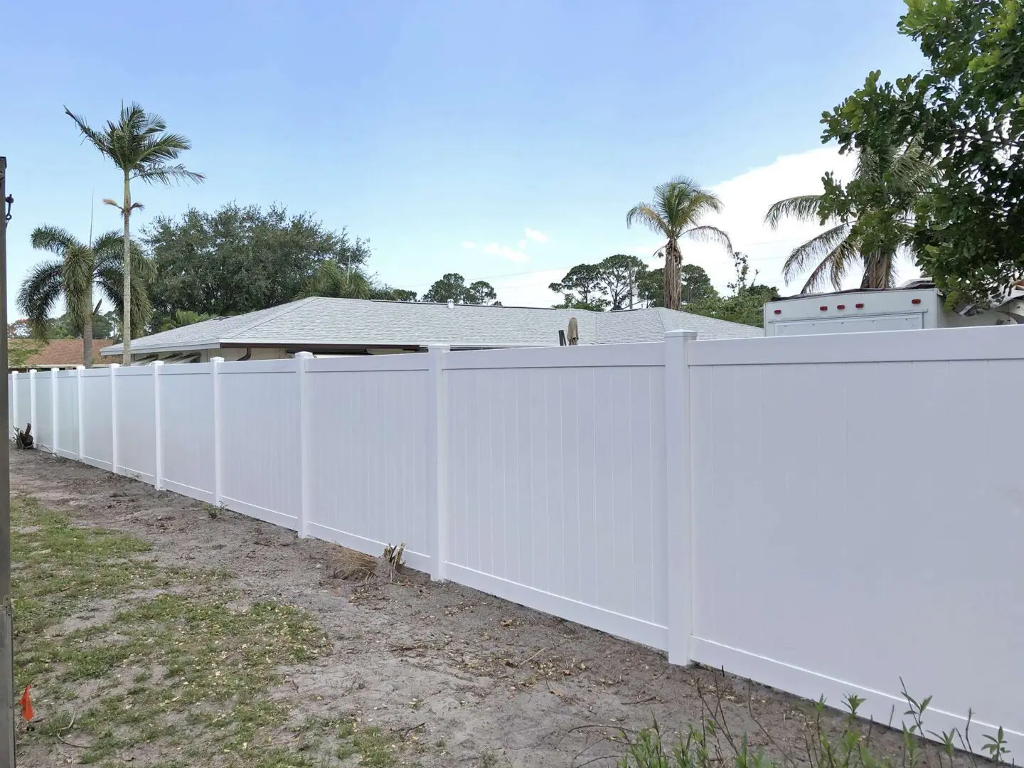 A white fence with palm trees in the background.