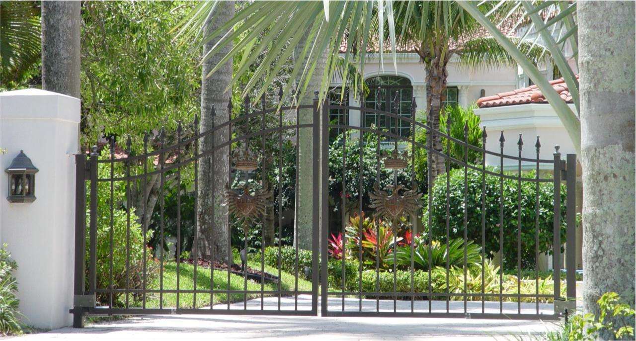 A gated driveway with palm trees and bushes.