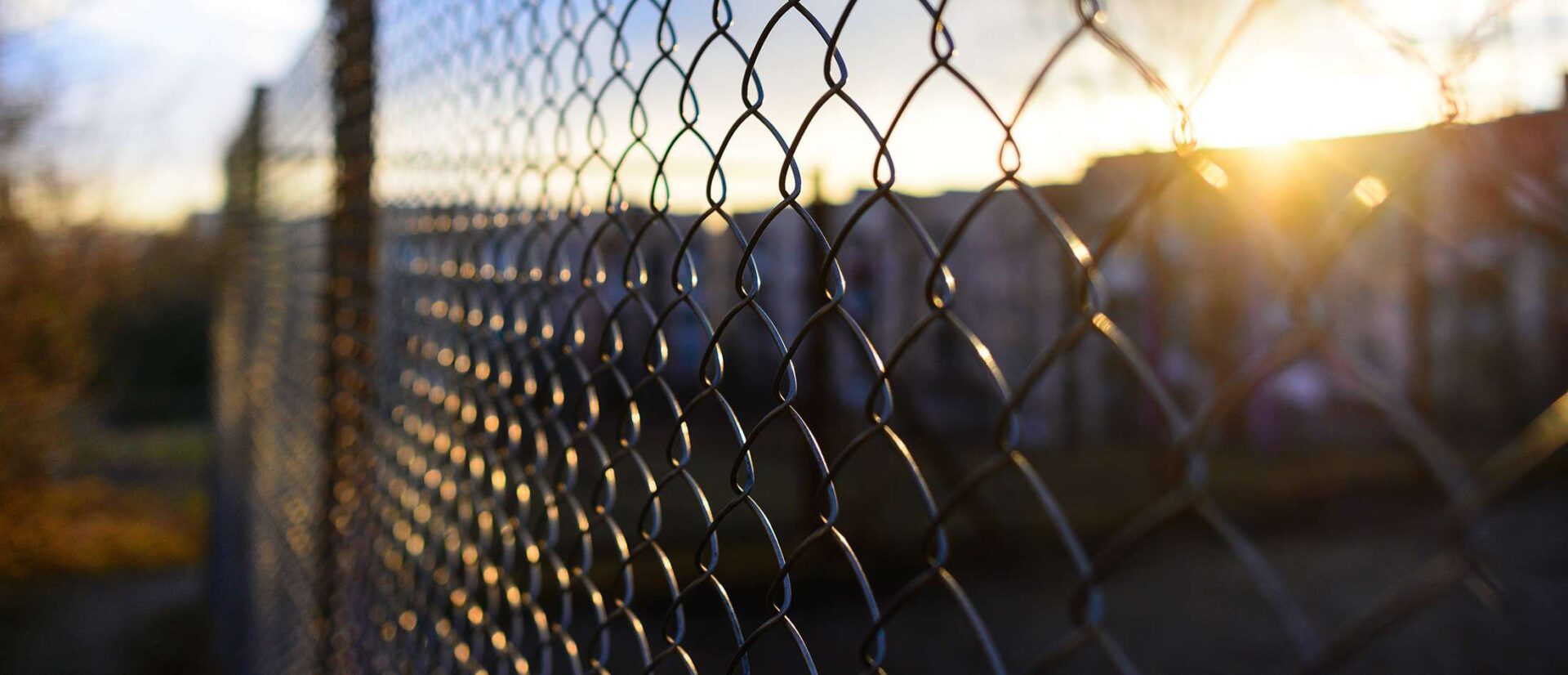 A chain link fence with the sun setting behind it.