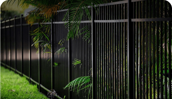 A black fence with green plants in the background.