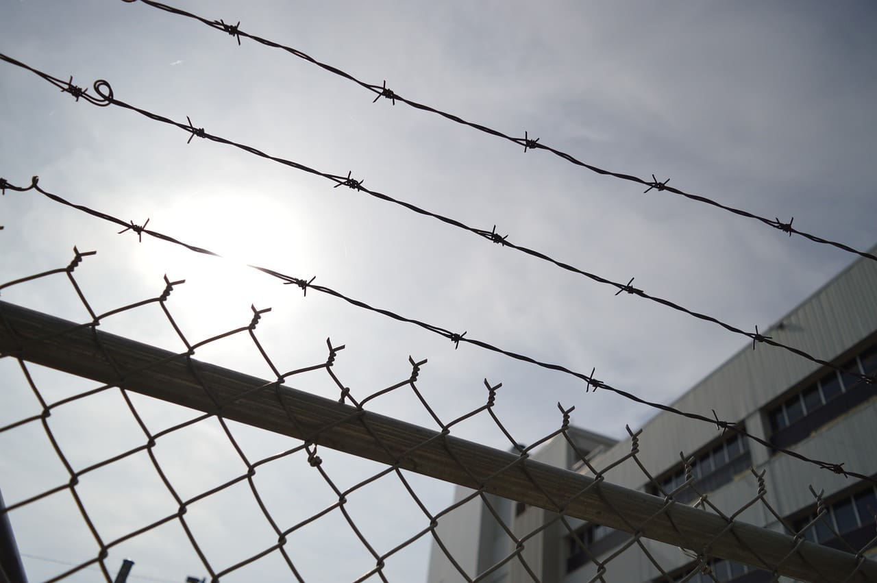 A fence with barbed wire and a building in the background.