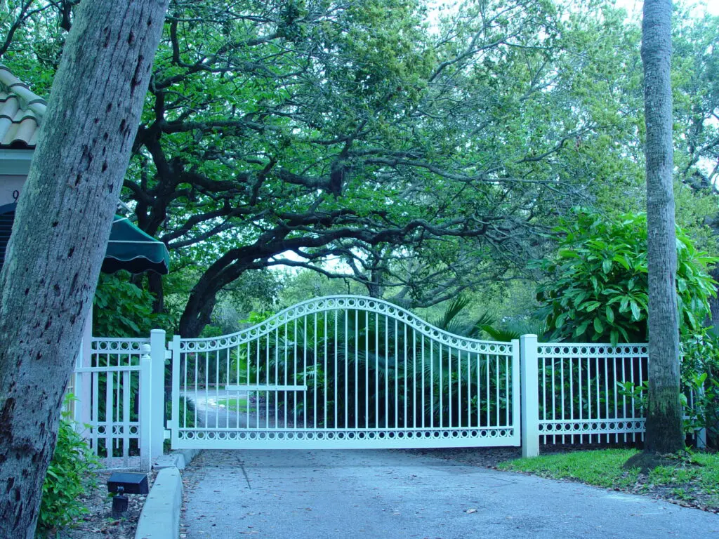 White gate and fence by leafy trees.