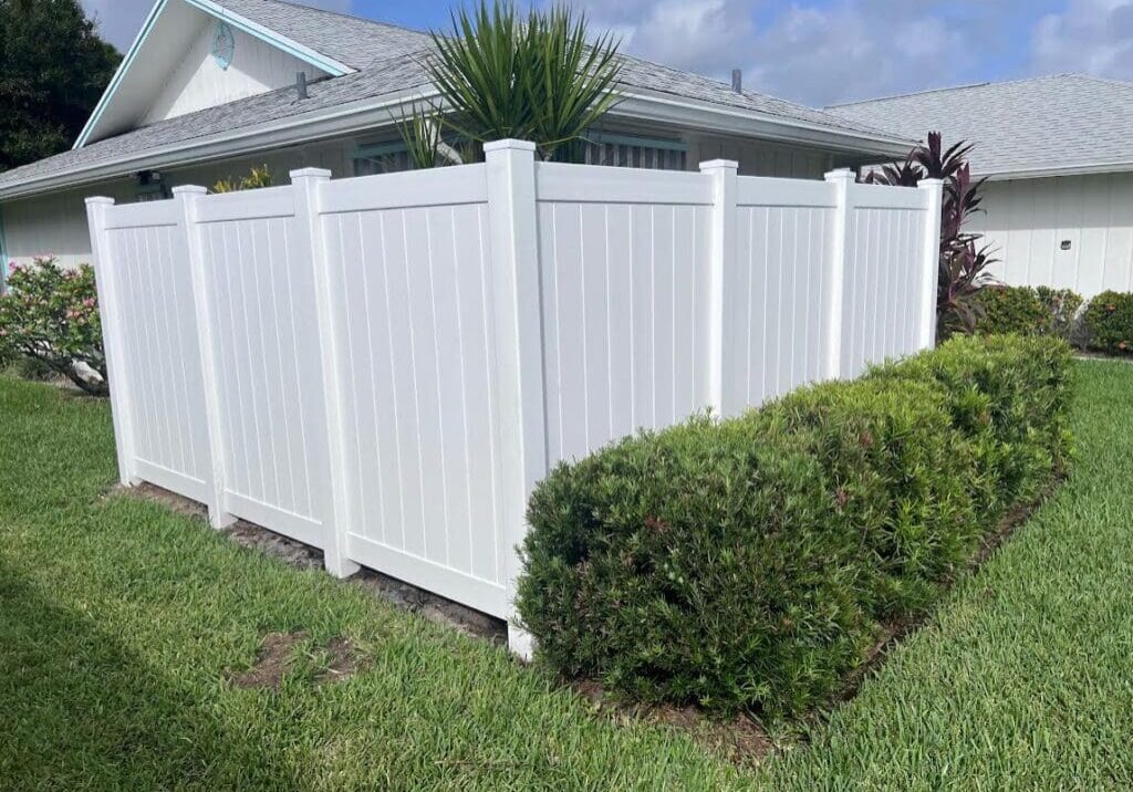 White vinyl fence with green shrubs.